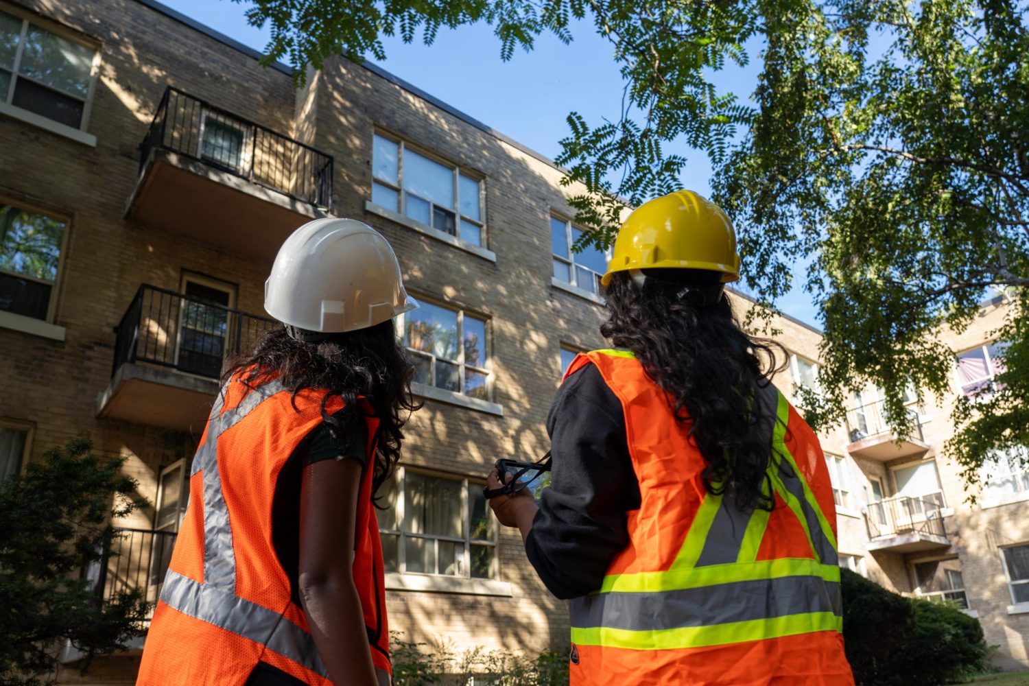 Two building professionals in safety vests looking up at a mid-rise building